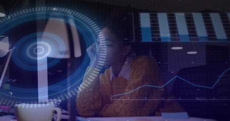 Analyzing digital charts, woman in yellow sweater leaning head on hand in office with coffee mug