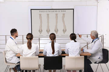Team of doctors using video projector during conference about scoliosis indoors. Illustrations on...