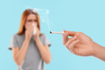 Obraz premium Passive smoking. Woman covering her nose with tissue because of man smoking nearby on light blue background. Selective focus