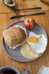 The plate showcases a wholesome breakfast with soft bread, juicy apple, sunny-side-up egg, and a warm tortilla, offering a colorful and nutritious start to the day.

