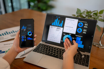 person is using a laptop and a cell phone to view graphs and charts