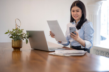 woman is sitting at a desk with a laptop and a cell phone