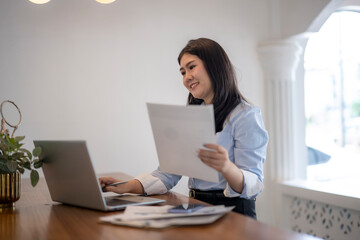 woman is sitting at a desk with a laptop and a stack of papers