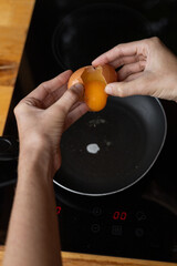 Detailed photo showing hands carefully holding a cracked egg above a hot pan as the golden yolk falls into the sizzling skillet, capturing the essence of fresh cooking in action

