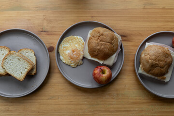Top-down photo featuring a sandwich, apple, and tortilla on a plate placed on a rustic wooden table, highlighting a natural, cozy atmosphere with fresh and wholesome food.

