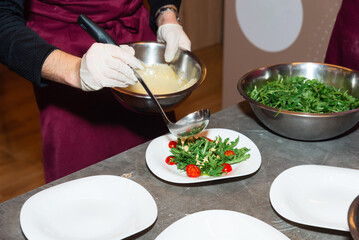 Chef plating arugula salad with dressing.
