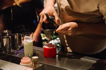 Bartender straining vibrant cocktail at bar.