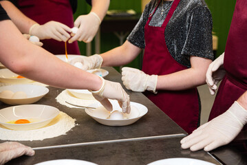 Cooking class students cracking eggs into flour.