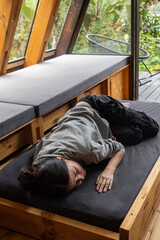 A young woman rests comfortably lying on a wooden bed frame that is pulled out from a drawer inside a stylish glamping tent. The scene blends rustic charm with modern outdoor luxury, capturing a peace