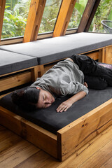 A tranquil young woman sleeps comfortably on her side atop a rustic wooden bed that pulls out from...