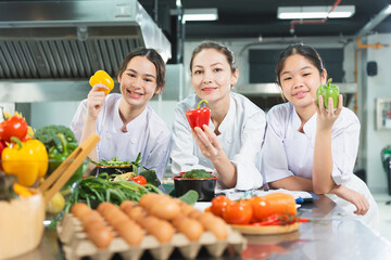 Young Chefs and Mentor with Fresh Vegetables in Culinary Class, Smiling Women in Chef Uniforms...
