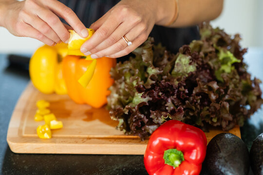 woman's hands removing seeds from yellow pepper, fresh veggies on wooden cutting board