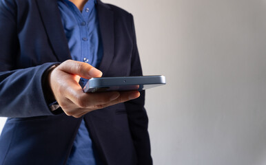  A close-up of an office worker's hand holding and looking at their phone, wearing business attire with blue shirt, grey background