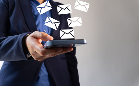 Close-up of a man's hand holding a smartphone with white email icons flying, representing the business email technology concept