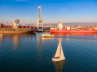 A sailboat navigates the waters near a docked container ship at the Port of Oakland, California,...