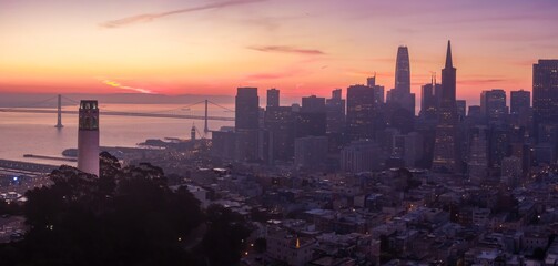 San Francisco, USA: Coit Tower and the Bay Bridge are silhouetted against a vibrant sunrise. The...