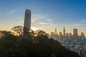Coit Tower stands tall as the sun rises over San Francisco, California, USA. The city skyline is...