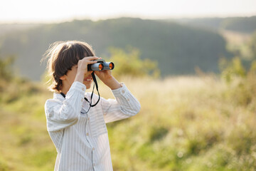 Little boy standing in a field with a binoculars at summer