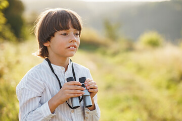 Little boy standing in a field with a binoculars at summer
