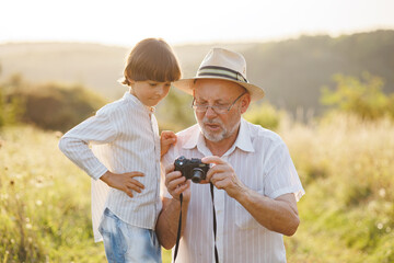 Little boy with his grandfather standing in a field with a camera at summer