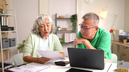 Elderly Asian couple focusing on laptop while reading paper documents and making decisions together - Powered by Adobe