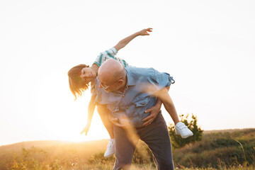 Photo of a senior man carrying a little boy piggyback in a field at summer