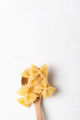 Top view of raw farfalle pasta on a wooden spoon placed on a white background, Bow-tie shaped pasta...