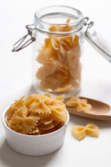 Raw farfalle pasta in a white bowl and glass jar on white background, Bow-tie shaped pasta highlighting Italian culinary ingredients
