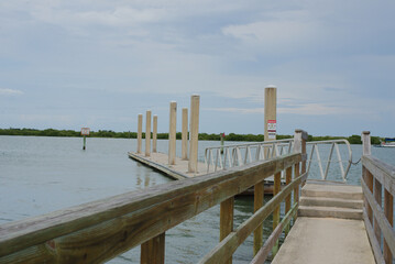 Fototapeta premium Dockside View of Sailboats Anchored on Serene Coastal Waters. A scenic view featuring a dock leading to a calm sea with moored sailboats under a blue sky, invoking feelings of relaxation and tranquili