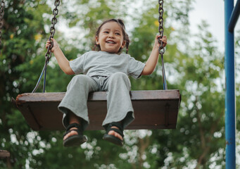 cheerful toddler girl playing on wooden swing at playground
