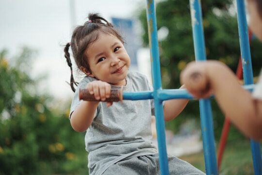 cheerful toddler girl playing on double swing with freind at outdoor playground