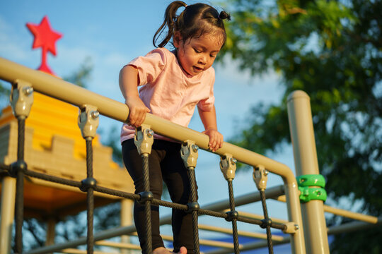happy toddler girl playing with climbing ropes net at a outdoor playground in park