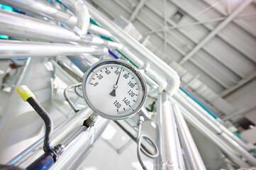 Round dial thermometer measures temperature in industrial piping system during processing hours in...