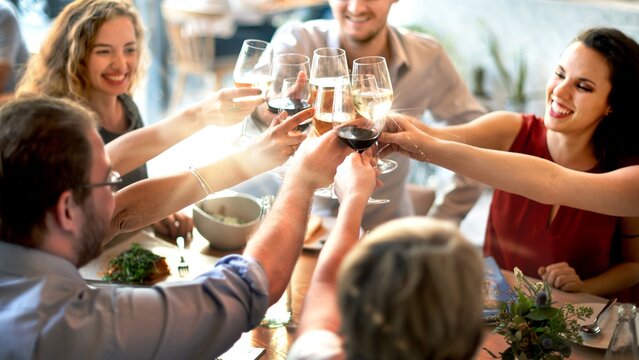 Diverse group celebrating with wine at a festive gathering. People enjoying a meal, raising glasses, sharing joy. Festive atmosphere with food and drinks. Diverse people toasting drinks celebrating