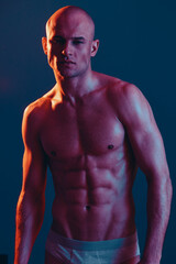 Fototapeta premium A striking image of a muscular man posing confidently in dramatic lighting, showcasing his physique with colorful contrasts and artistic flair. Perfect for fitness themes.