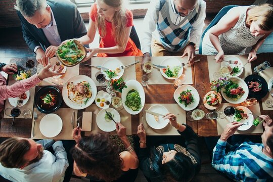 Diverse group dining together, sharing food, enjoying a meal. Mixed ethnicities, men and women, social gathering, vibrant table setting, communal dining experience. Celebration and gathering.