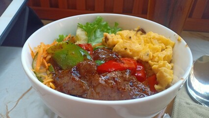 A delicious plate of black pepper barbecue beef served over steamed rice, accompanied by scrambled...