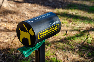  a cylindrical dog waste bag dispenser in a suburban park in Australia with a polite message...