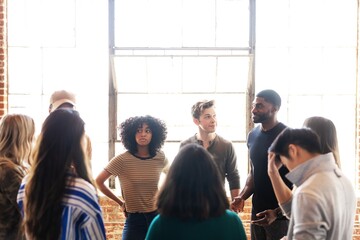 Group of diverse people in casual attire having a discussion in a bright room. They stand in a...