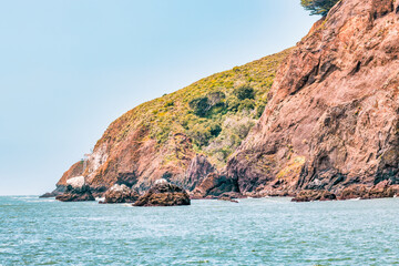 Kirby Cove Beach in California with red sand, blue ocean waves, and dramatic cliffs covered in pine trees. A hidden gem near San Francisco, perfect for nature, travel, and coastal exploration themes
