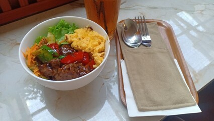 A delicious plate of black pepper barbecue beef served over steamed rice, accompanied by scrambled...