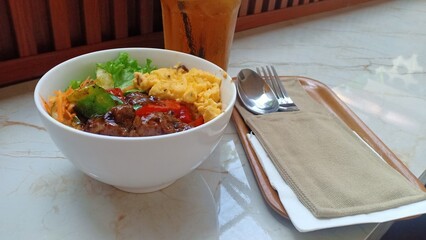 A delicious plate of black pepper barbecue beef served over steamed rice, accompanied by scrambled...