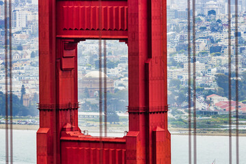 Close-up of Golden Gate Bridge tower with Palace of Fine Arts in the background, San Francisco cityscape and boats on the bay visible through the iconic red structure.