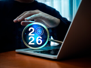 Happy new year 2026, success with artificial intelligence tools technology concept. 2026 calendar numbers with target icon and AI circuit graphics in magnifying glass while man work with computer.