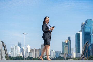 Confident Asian businesswoman using smartphone while walking in modern city. Professional female...