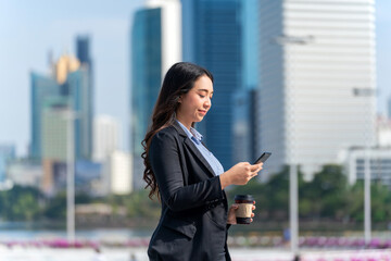 Asian businesswoman using phone in central business district. Businesswoman holding coffee and...