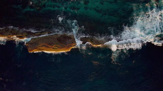 Morning sun casts warm light on a rock surrounded by shallow sea water. Gentle waves lap softly against the rock&rsquo;s edges in this tranquil coastal scene, captured with drone in NSW