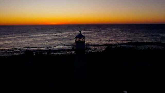 Drone flies over Warden Head Lighthouse at sunrise near Ulladulla, NSW. A bird takes off as the golden sun rises on the horizon, capturing a serene moment of coastal beauty and freedom.