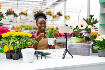 A woman broadcasts from a garden center. She is surrounded by flowers and plants.