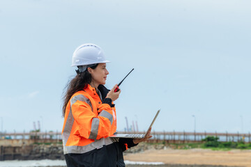 Profile view of a female engineer reporting status via radio at a logistics and shipping terminal....